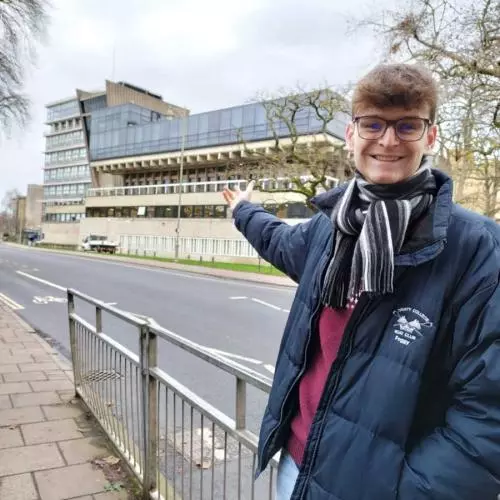 Thomas Fogg proudly pointing to the Denys Wilkinson Building where he completed his award-winning MPhys project on the innovative GaToroid particle therapy system.
